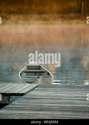 Canoe tied to dock at sunrise with mist on lake Stock Photo