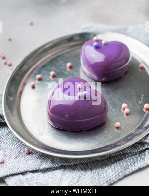Vertical selective closeup shot of purple dessert in the shape of hearts on a gray oval tray Stock Photo