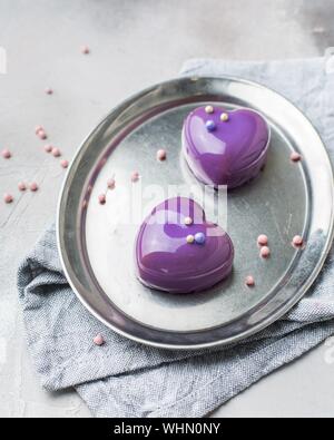 Vertical selective closeup shot of purple dessert in the shape of hearts on a gray oval tray Stock Photo