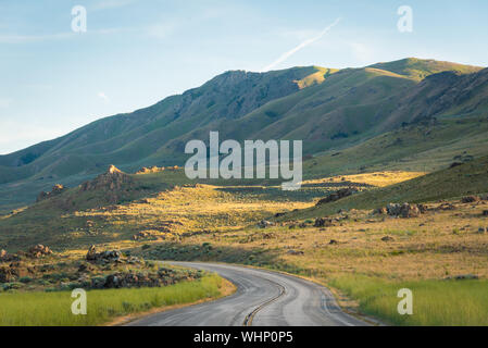 Road with grassy fields and mountains at Antelope Island State Park, Utah Stock Photo