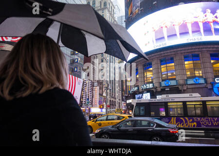 A woman with an umbrella is crossing a busy road in Times Square during a rainy day. Stock Photo