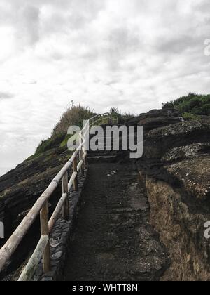 Stone stairway towards the top of the hill with wooden railing under cloudy gray sky after the rain Stock Photo