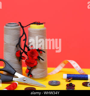 Two large spools of thread are standing, many small spools are lying. Large scissors for sewing, but the photo has buttons and a measuring tape. Needl Stock Photo