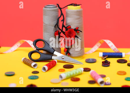 Two large spools of thread are standing, many small spools are lying. Large scissors for sewing, but the photo has buttons and a measuring tape. Needl Stock Photo