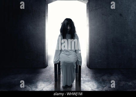 Scary ghost woman with blood and dirty face sitting in the dark room. Halloween concept Stock Photo