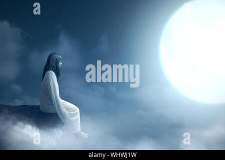 Scary ghost woman with blood and dirty face sitting on the rock with moonlight. Halloween concept Stock Photo