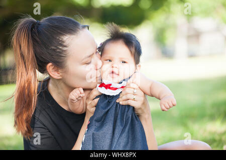 Young Caucasian/Asian mother kissing happy Asian 1 yo daughter Stock Photo