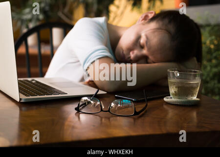 Tired young woman sleeping on her computer desk. Stock Photo