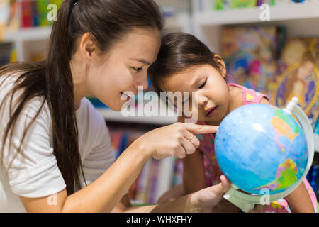 A teacher and a preschool student learning geography on a world globe Stock Photo