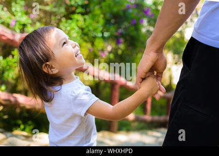 Little girl holding her father's hand smiling at him, while taking a walk together Stock Photo