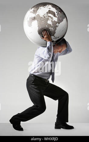 Full length side view of a businessman struggling to carry globe on shoulders against gray background Stock Photo