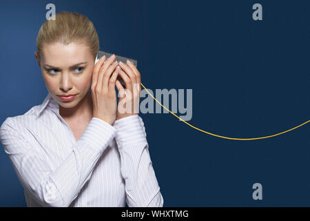 Businesswoman listening to tin can phone against blue background Stock Photo