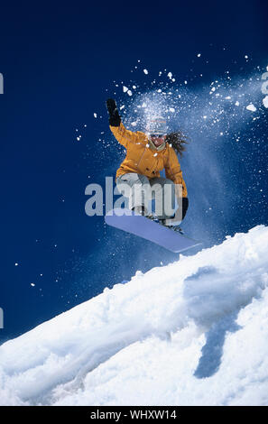 Low angle view of a snowboarder in midair above ski slope with snow powder trailing behind Stock Photo