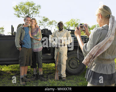 Couple and safari guide posing by jeep while young woman taking photograph Stock Photo