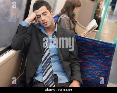 Businessman with loosened tie sleeping in commuter train Stock Photo