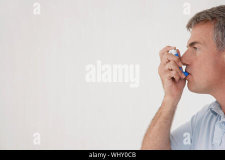 Side view of middle aged man using inhaler isolated on white background Stock Photo