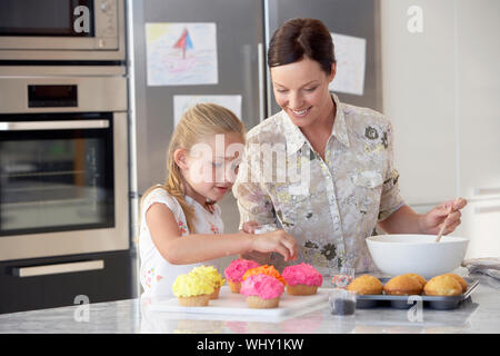 Happy mother and daughter preparing cupcakes in kitchen Stock Photo
