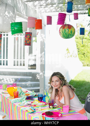 Young mother sitting at messy outdoor table after birthday party Stock Photo