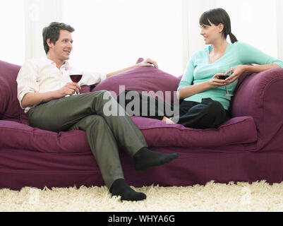 Happy young couple with wineglasses relaxing on sofa Stock Photo