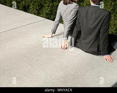 Midsection of young business couple sitting on wall outdoors Stock Photo