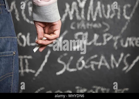 Closeup of man holding chalk standing in front of blackboard Stock Photo