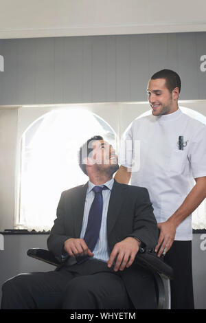Young hairdresser preparing businessman for haircut in barber shop Stock Photo