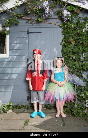 Full length portrait of a young boy in pirate costume and girl in fairy costume by shed Stock Photo
