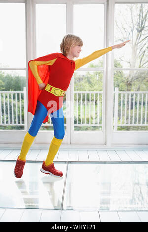 Full length of a young boy in superhero costume with arm extended indoors Stock Photo
