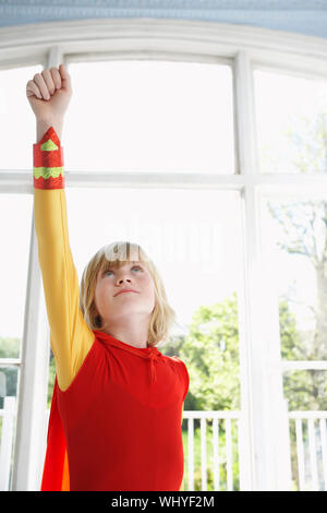 Serious young boy in superhero costume with raised fist looking up Stock Photo