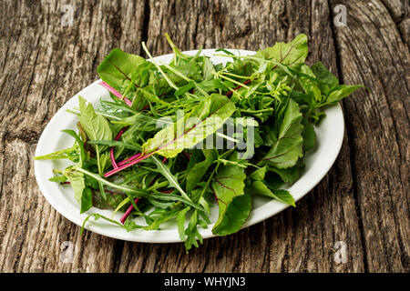 Fresh salad plate with mixed greens arugula, mesclun, mache on dark wooden background close up. Healthy food. Green meal. Stock Photo