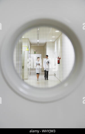 View from window in door of male and female scientists walking down hallway Stock Photo