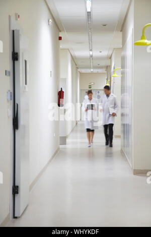 Full length of male and female scientists walking down hallway Stock Photo
