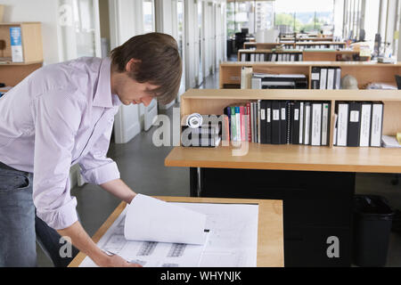 Side view of a young male architect studying blueprint in office Stock Photo