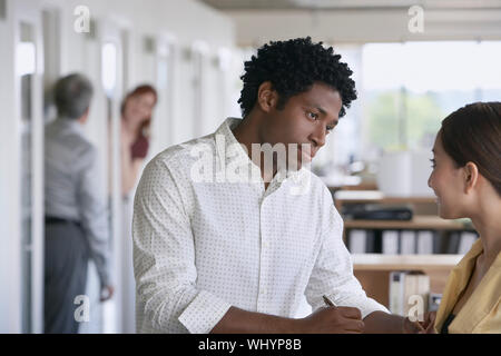 Businessman and colleague talking in office with blurred coworkers in background Stock Photo