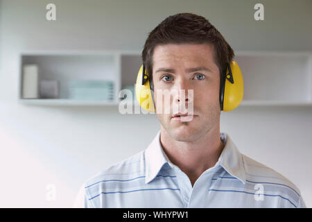Closeup portrait of a young man wearing ear protectors in office Stock Photo