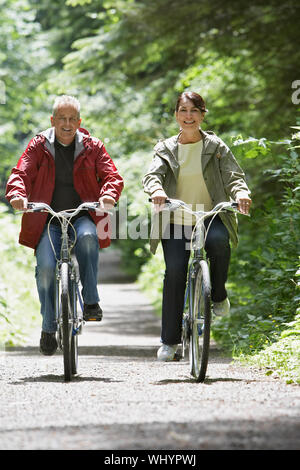 Full length of a mature man and middle aged woman biking on forest road Stock Photo