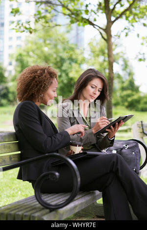Two young businesswomen working on park bench Stock Photo