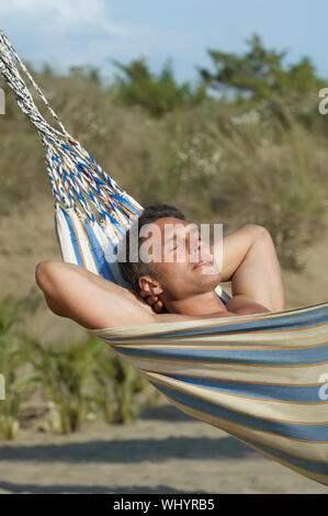View of a man relaxing in hammock against blurred plants Stock Photo
