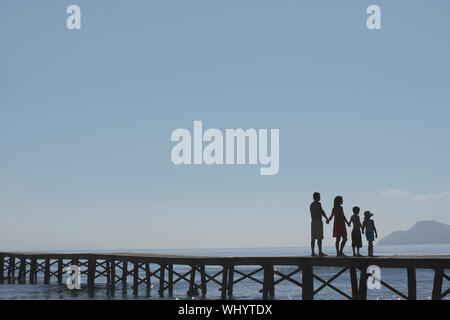 Full length of silhouetted parents and two children holding hands on jetty Stock Photo