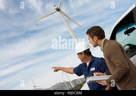 Engineers examining wind turbines by car at wind farm Stock Photo