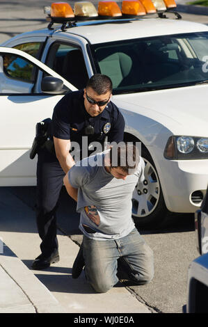 A mature police officer arresting young man on road side for breaking traffic rules Stock Photo