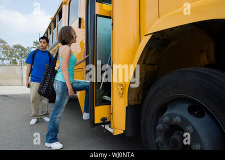 Young female student getting on school bus with classmate standing by it Stock Photo