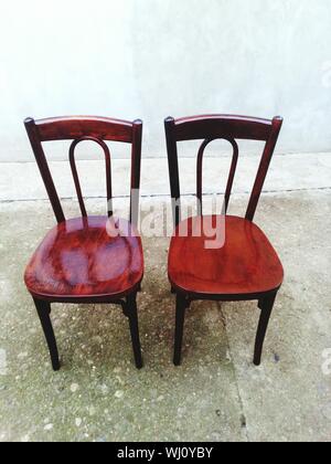 Close-up Of Empty Chairs On Footpath Against Wall