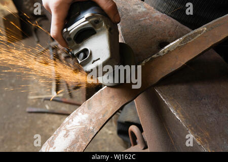 Blacksmith using angle grinder on edge of metal tool in workshop Stock Photo