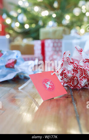 Unwrapped gift paper and tag on hardwood floor with Christmas tree in background Stock Photo