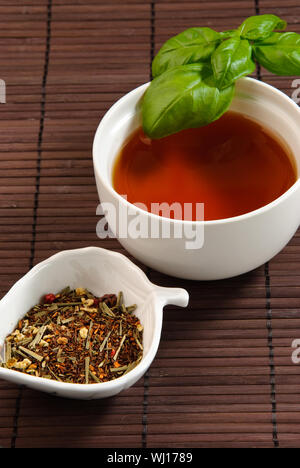 cup of tea with basil leaves on a bamboo mat with tea leaves Stock Photo
