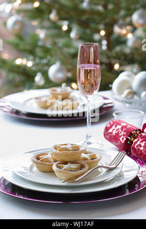 Christmas mince pies; cracker and champagne flute on dining table Stock Photo