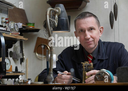 Portrait of confident middle aged repairman working on clock in workshop Stock Photo