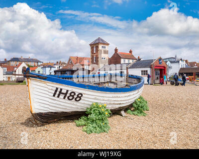 16 June 2019: Aldeburgh, Suffolk, UK - Old boat on the beach, with the RNLI Lifeboat Station and people sightseeing. Sunny summer day. Stock Photo