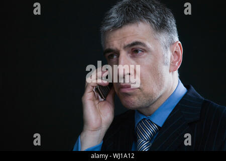 Closeup of a serious and worried businessman using cellphone against black background Stock Photo
